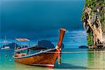 A Thai boat with a long tail near the shore, a blue rain cloud over the Andaman Sea