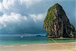 A large high cliff in the sea, rain clouds over the sea. White yacht is standing by the shore