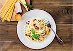 Pasta Carbonara. Spaghetti with bacon and parmesan cheese. Pasta Carbonara on white plate with parmesan on dark background and ingredients. Italian food concept. Top view.
