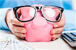 Pig stuffed with money in the hands of an economical woman close-up with glasses