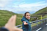 Young laughing girl outstretching hand asking to follow her on background of mountain road, Iceland, West Fjords.