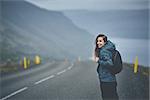 a woman tourist wearing in warm outdoor clothing on the empty road on the fjord in Iceland