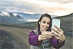 Girl in warm clothing makes selfie photo on background of mountains and sea of Iceland. women on the road thru a mountain pass, fjord is on background