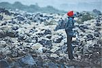 Woman in waterproof clothing walks on volcanic Lava fields on background of mountains of Iceland.