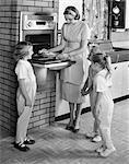 1950s MOTHER AND THREE DAUGHTERS STANDING AROUND OVEN IN KITCHEN BAKING PIE