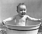 1920s 1930s SMILING HAPPY WET BABY GIRL SITTING BATHING IN METAL WASH TUB