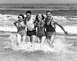 1930s TWO COUPLES MEN WOMEN LAUGHING RUNNING IN OCEAN SURF WAVES