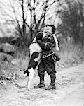1950s SMILING BOY WEARING WINTER COAT HAT SCARF BOOTS ICE SKATES SLUNG OVER SHOULDER HUGGING ENGLISH SPRINGER SPANIEL DOG