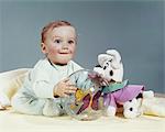 1960s WIDE-EYED BABY CHILD LOOKING AT CAMERA PLAYING WITH TOYS STUFFED ANIMAL AND PLASTIC BALL