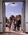 1960s FAMILY OF FIVE WALKING IN THE FRONT DOOR OF CHURCH LOOKING AT CAMERA