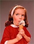 1960s CUTE EXPRESSION BRUNETTE LITTLE GIRL WEARING A RED DRESS EATING ICE CREAM CONE