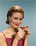 1960s SMILING WOMAN WEARING EVENING DRESS AND JEWELRY HOLDING MARTINI COCKTAIL GLASS LOOKING AT CAMERA