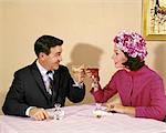 1960s COUPLE TOASTING EACH OTHER WITH WINE IN RESTAURANT WOMAN WEARING FLOWERED HAT