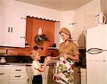 1970s BLONDE MOTHER GIVING SON GLASS MILK IN KITCHEN