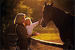 1980s BACKLIT SILHOUETTED BLOND WOMAN MOTHER HOLDING CHILD DAUGHTER REACHING OUT TO TOUCH HORSE