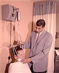 1950s 1960s MAN TECHNICIAN ADJUSTING TENSION ON WOMAN PATIENT CHIN BRACE NECK TRACTION MEDICAL EQUIPMENT