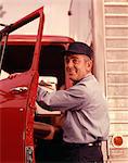 1950s 1960s SMILING MAN DELIVERY DRIVER WEARING CAP AND UNIFORM LOOKING AT CAMERA STEPPING INTO CAB THROUGH OPEN TRUCK DOOR