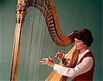 1960s WOMAN PLAYING LARGE GOLDEN CONCERT OR PEDAL CHROMATIC HARP