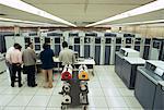 1970s SMALL GROUP OF MEN TECHNICIANS IN MAINFRAME COMPUTER ROOM WITH MULTIPLE MAGNETIC TAPE DRIVE MACHINES