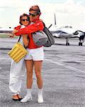 1980s UPSCALE COUPLE ON TARMAC PRIVATE PLANE WEARING SPORTY TENNIS CLOTHES HUGGING