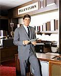 1960s SALESMAN STANDING IN TELEVISION SECTION OF DEPARTMENT STORE LOOKING AT CAMERA