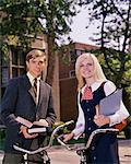 1960s PORTRAIT STUDENT COUPLE ON CAMPUS WITH BIKES AND BOOKS LOOKING AT CAMERA