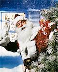 1950s 1960s 1970s SANTA CLAUS WITH PACK OF PRESENTS TOYS WAVING IN SNOW IN FRONT OF HOUSE OUTDOOR CHRISTMAS