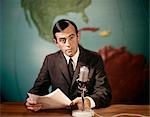 1960s NEWSMAN NEWS ANCHOR READING NEWS FROM PAPERS SPEAKING INTO MICROPHONE LOOKING AT CAMERA