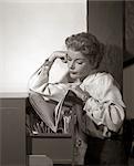 1950s 1960s DISTRACTED OFFICE SECRETARY FILE CLERK LEANING ON ELBOW ON METAL FILING CABINET LOOKING INTO FILE FOLDER