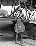 1920s FEMALE AVIATOR AVIATRIX LEATHER COAT CAP WITH GOGGLES AND LACE UP BOOTS PREPARING TO BOARD SEAPLANE