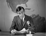 1960s 1970s NEWSMAN READING NEWS FROM PAPERS LOOKING AT CAMERA SPEAKING INTO MICROPHONE WORLD MAP BEHIND