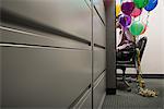 Businessman sat with balloons tied to his chair