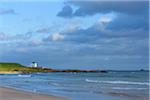 Beach along the North Sea in Bamburgh with the Bamburgh Lighthouse in the distance in Northumberland, England, United Kingdom