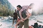 Young man carrying friend over shoulder on riverside, Lombardy, Italy