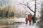 Rear view of adult friends with bouldering mat backpack walking along riverside, Lombardy, Italy