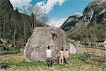 Rear view of adult bouldering friends watching young woman climb boulder, Lombardy, Italy