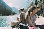 Two young adult hikers sitting by mountain lake, Lombardy, Italy