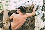 Rear view of bare chested male boulderer climbing boulder edge, Lombardy, Italy