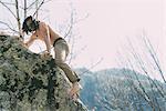 Bare chested and bare foot male boulderer climbing boulder, Lombardy, Italy