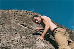 Low angle view of bare chested young male boulderer climbing boulder, Lombardy, Italy