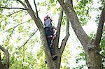 Young male trainee tree surgeon looking up from tree trunk