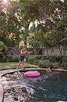 Children swimming in garden pool, young boy jumping in, mid-air