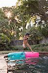 Young girl jumping into outdoor swimming pool, mid-air