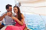 Couple sitting on boat, on water, holding champagne flutes, smiling