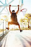 Young man on basketball court, swinging on basketball net frame, rear view