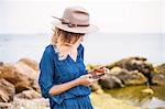 Mid adult woman in coastal setting, looking at smartphone