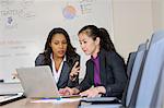 Two businesswomen in office, looking at laptop screen