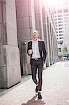 Cool businessman with takeaway coffee strolling along sidewalk, New York, USA