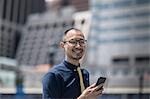 Portrait of smiling businessman with smartphone outside office building, New York, USA