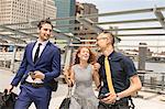 Businessmen and woman with luggage walking and talking on waterfront, New York, USA